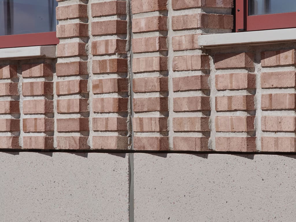 De opgeleverde gevel van Xplore: baksteen met verticaal reliëf en rode kozijnen