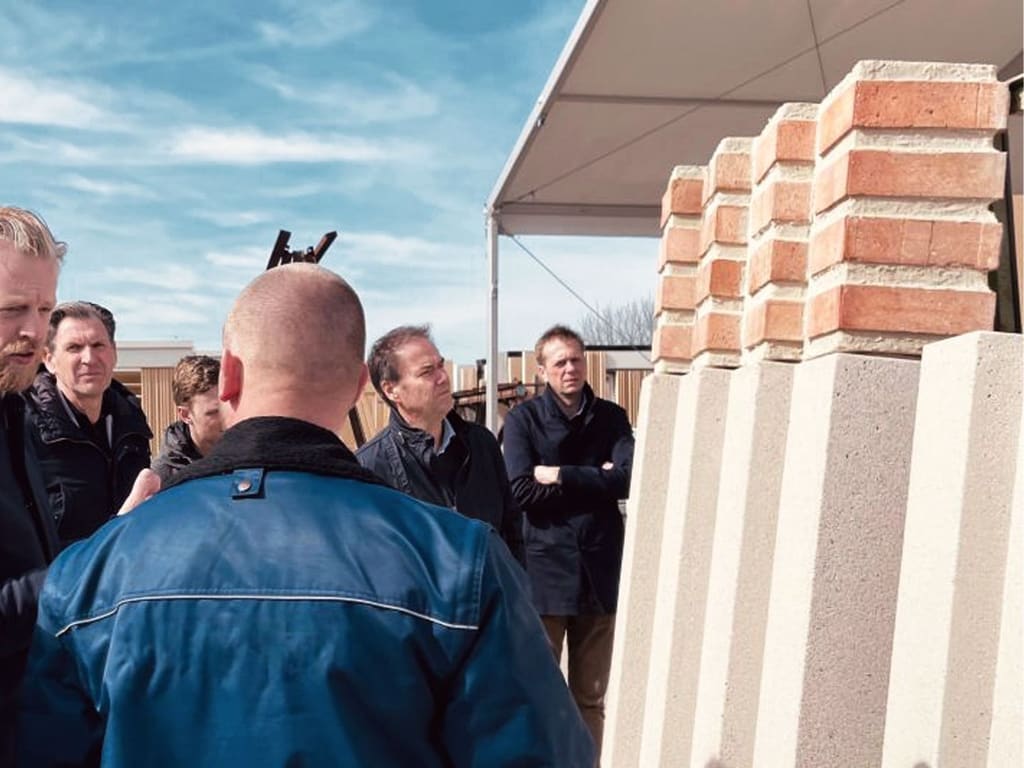 De gevel-mock-up van Xplore op ware grootte bij Hibex, met het team van de studio en de bouwers ervoor