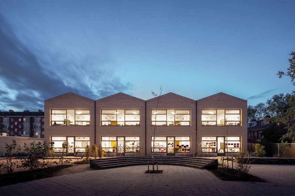 Basisschool Veerkracht bij schemering: vier huisvormige lokalen in lichte baksteen met verlichte ramen aan het schoolplein